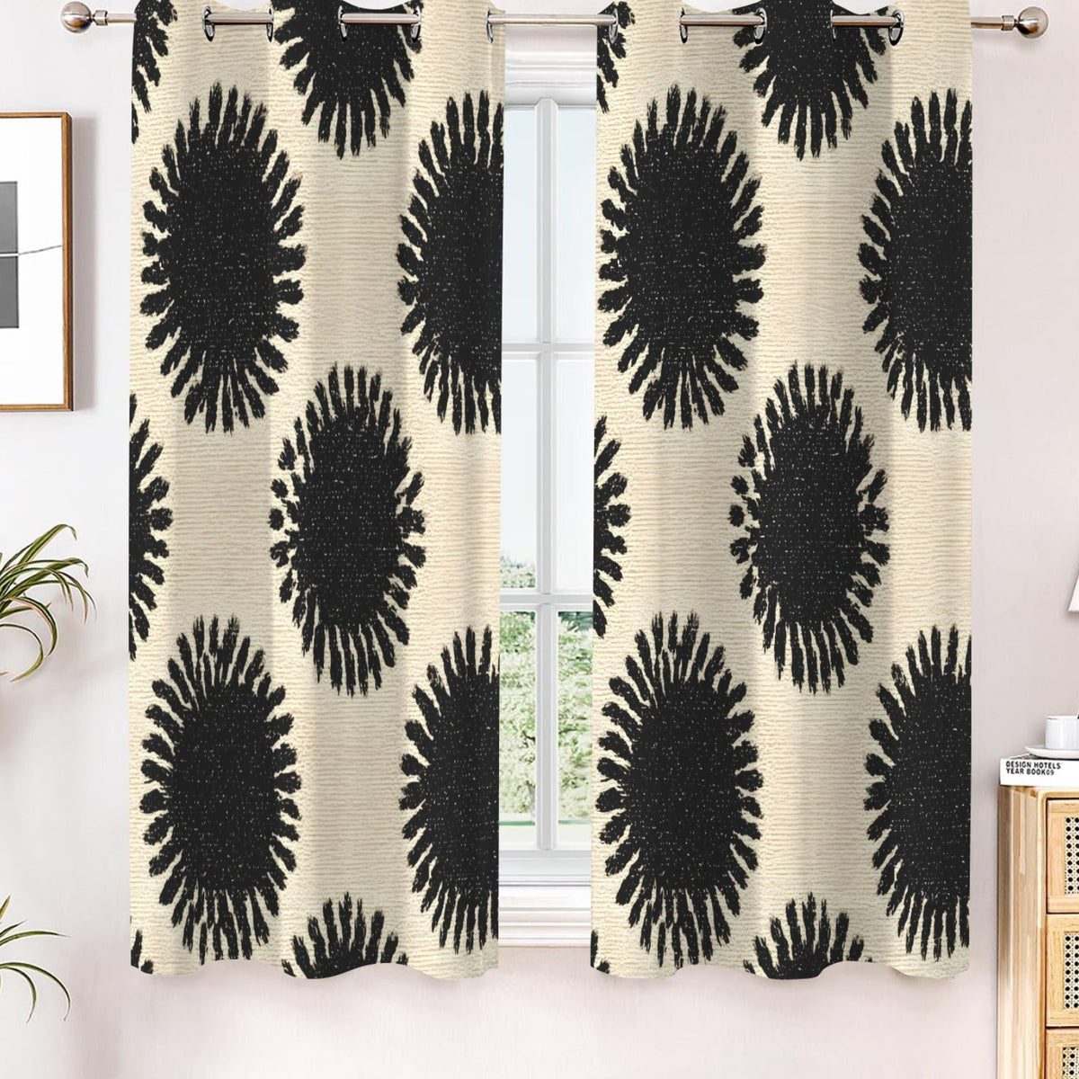 A pair of window curtains hanging on a silver rod in a styled room. The curtains have a textured cream background with a bold black circular sunburst pattern.