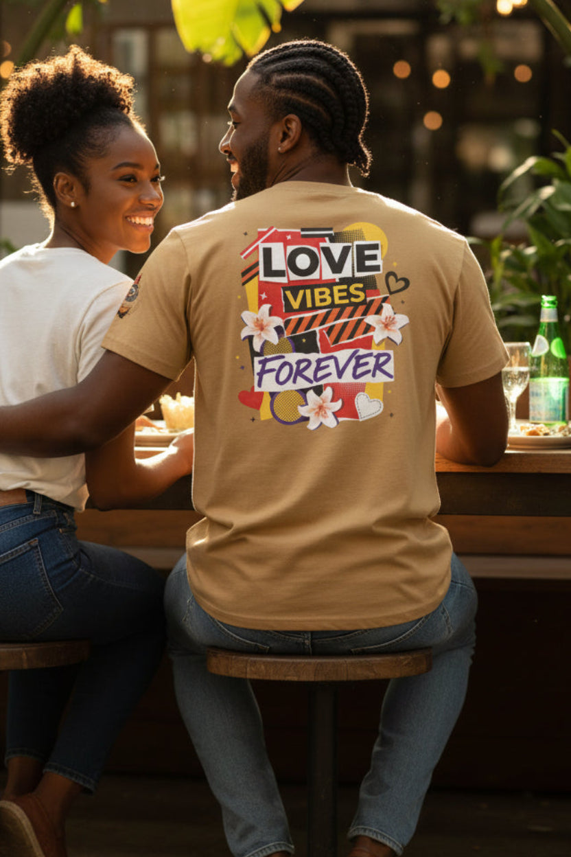 Two people sitting at an outdoor table with a person wearing a shirt with 'LOVE VIBES FOREVER' text.