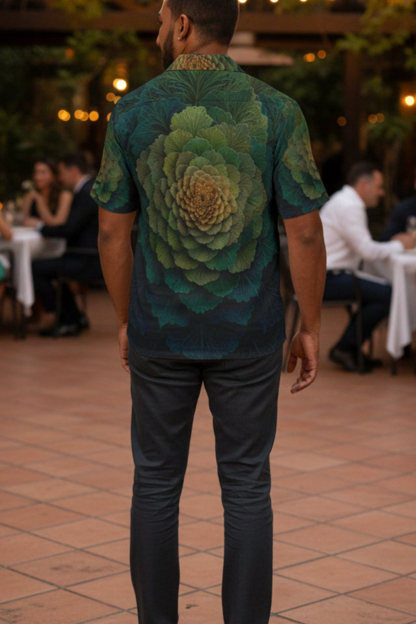 Man wearing a shirt with a green floral pattern in an outdoor setting with people sitting at tables.