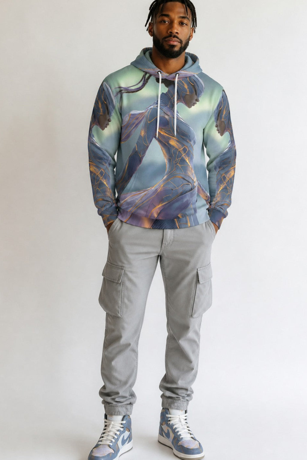 A man modeling a light blue and purple abstract-patterned hoodie, paired with gray cargo pants and blue and white sneakers, standing against a plain light gray background.