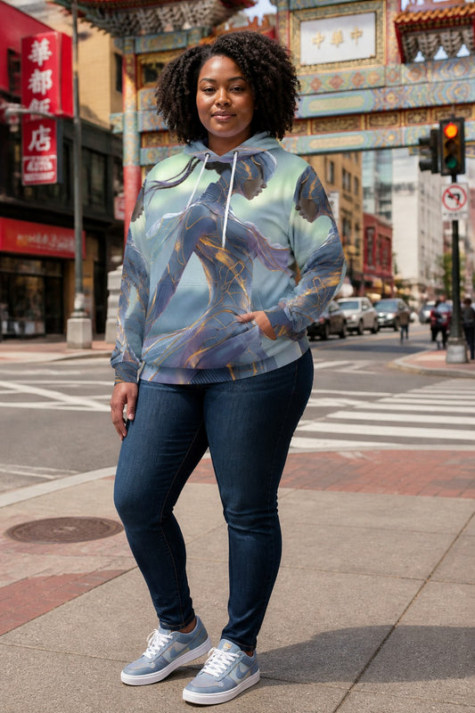A woman stands on a city street corner wearing a light blue and gray hooded sweatshirt with a detailed fantasy character print, paired with dark blue jeans and gray sneakers.