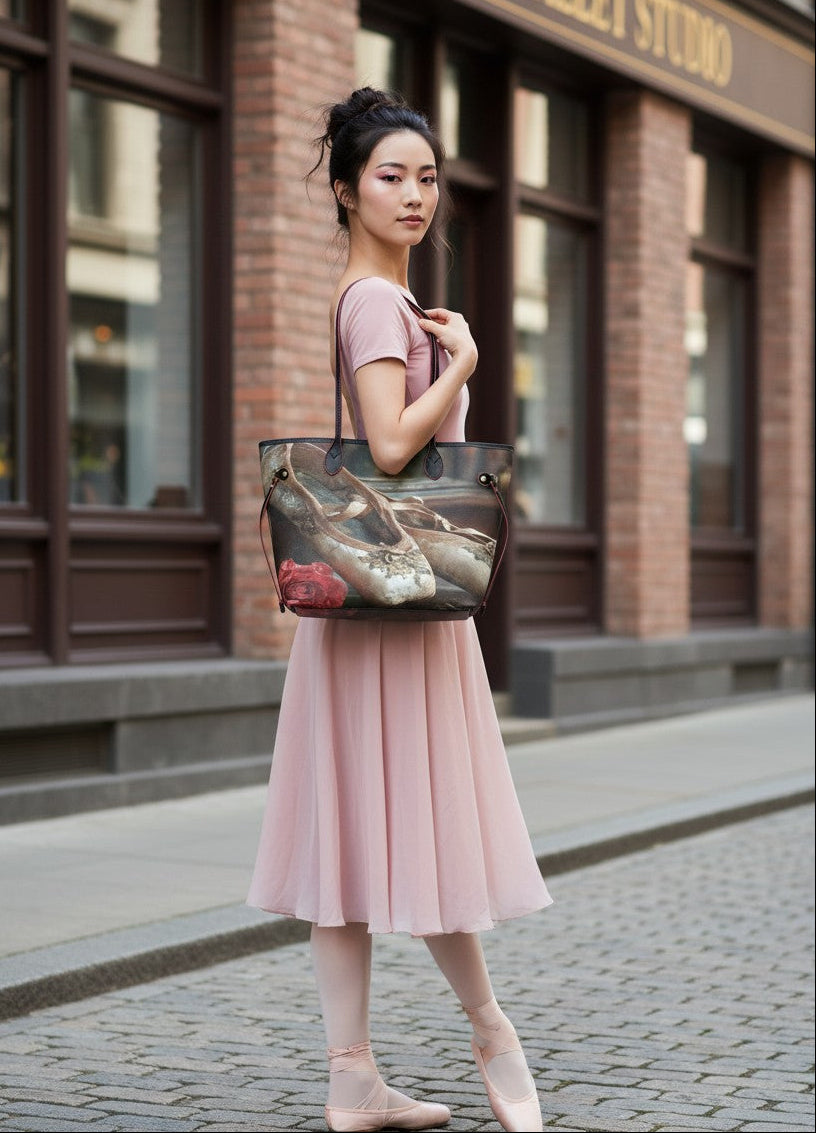 A woman in a pink ballet dress and pointe shoes stands on a cobblestone street in front of a brick building, carrying a large tote bag with a realistic fish print.