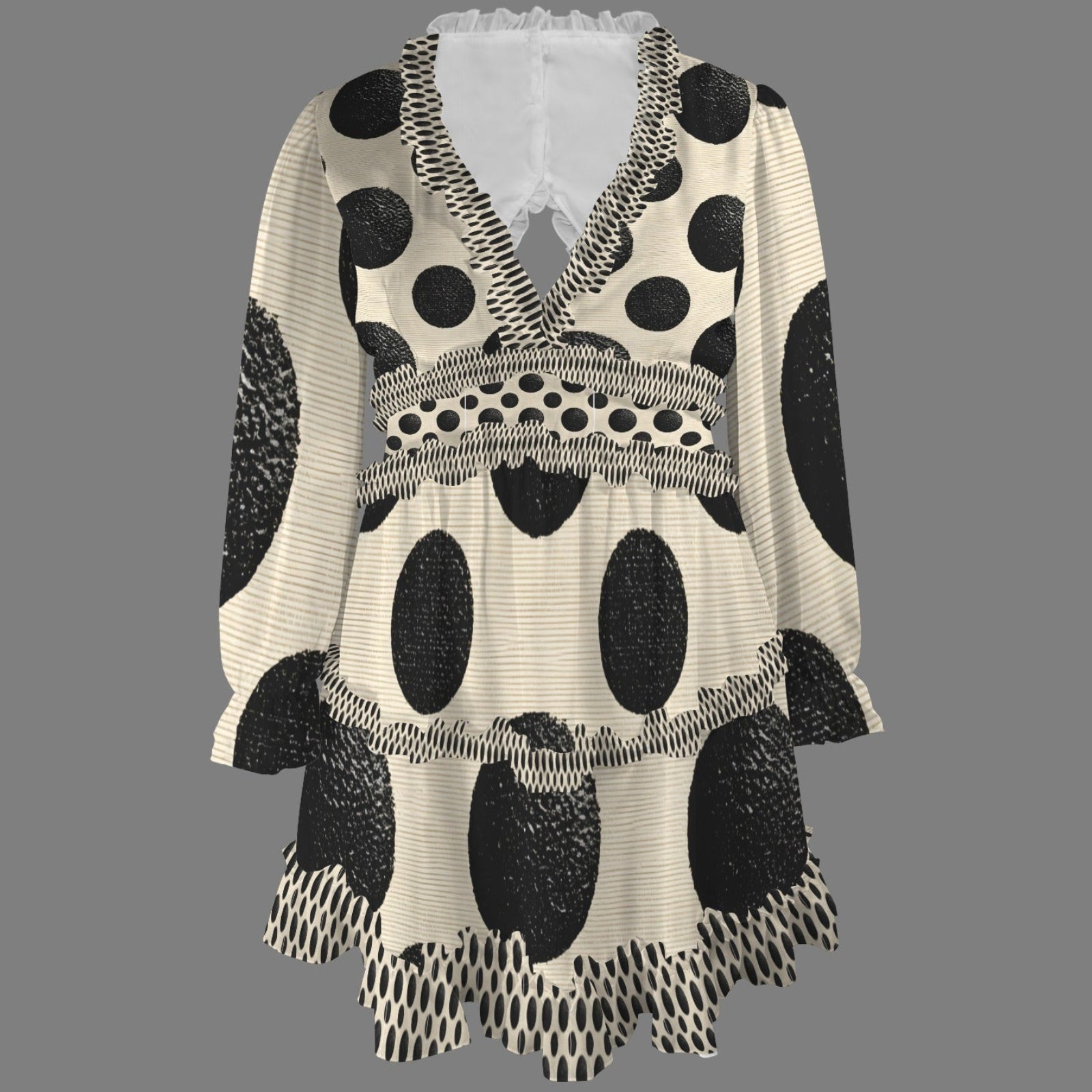 A women's long-sleeve V-neck tunic top with a black and off-white polka dot pattern, featuring textured black spots, ruffled trim, and a tiered hem, shown against a solid gray background.