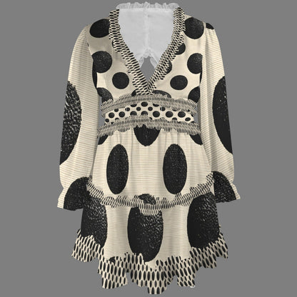 A women's long-sleeve V-neck tunic top with a black and off-white polka dot pattern, featuring textured black spots, ruffled trim, and a tiered hem, shown against a solid gray background.
