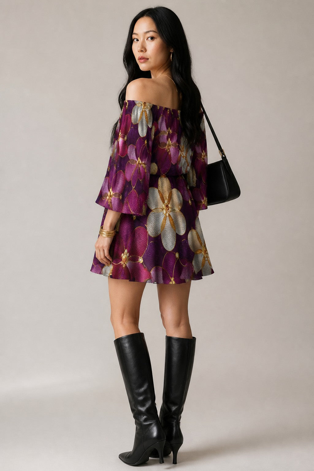 A woman modeling an off-the-shoulder purple floral mini dress with long ruffled sleeves, paired with black knee-high boots and a black shoulder bag, against a neutral studio background.