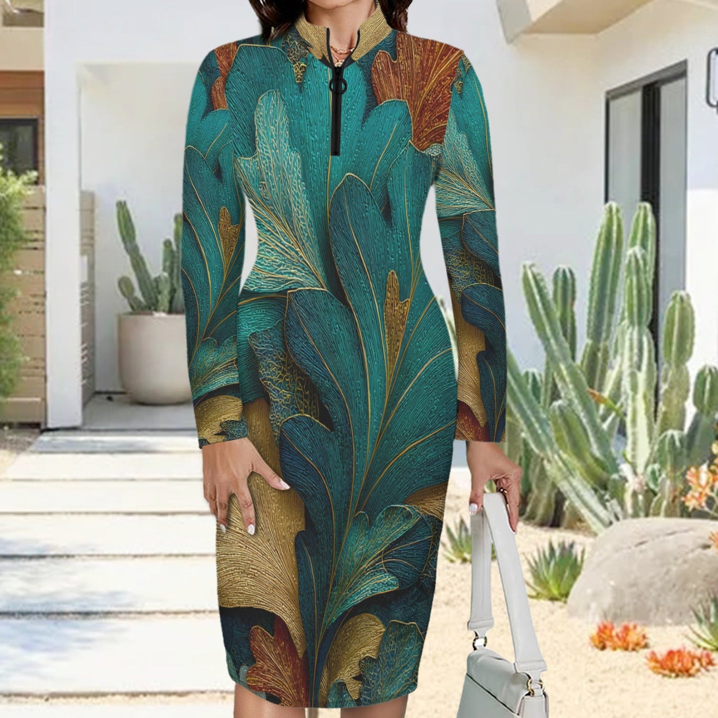 A woman models a long-sleeve, high-neck, half-zip bodycon dress featuring a large-scale abstract leaf pattern in teal, green, brown, and gold tones. She is standing in a sunny outdoor patio setting with cacti and holding a white handbag.