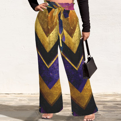 A person wearing wide-leg drawstring pants with a bold chevron pattern in gold, purple, and black, holding a small black handbag against a white wall.