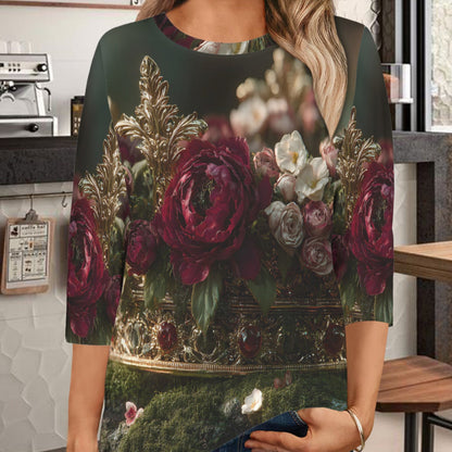 A woman wearing a three-quarter sleeve top with a dark green background and a large floral print featuring red and pink roses, photographed in a cafe setting.