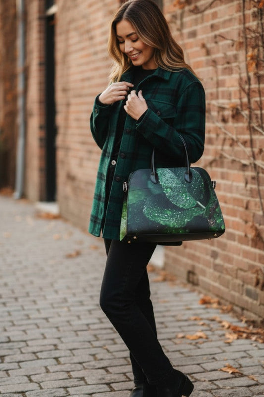 A woman stands on a brick sidewalk drinking from a white coffee cup while wearing a dark green plaid flannel shirt jacket, black pants, and black ankle boots. She is carrying a black tote bag with a green glittery leaf pattern.