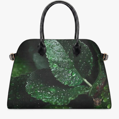 A structured black handbag with a glossy finish, featuring a printed design of green leaves covered in water droplets on the front panel. It has two black top handles and small gold-tone side hardware, shown against a plain light gray background.