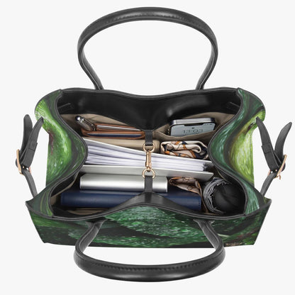 A green and black patterned tote bag shown open from above, with black leather handles and straps, and contents including papers, a wallet, and a rolled item visible inside, on a light gray background.