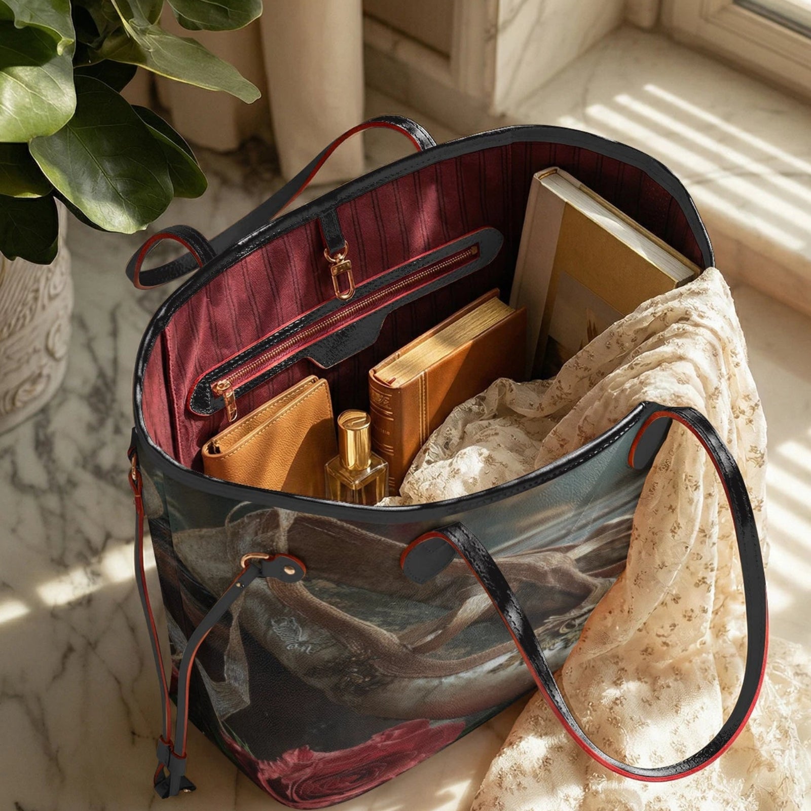 A tote bag with a dark blue and gray scenic print, red trim, and a burgundy interior, styled with books, a scarf, and a perfume bottle on a marble windowsill.