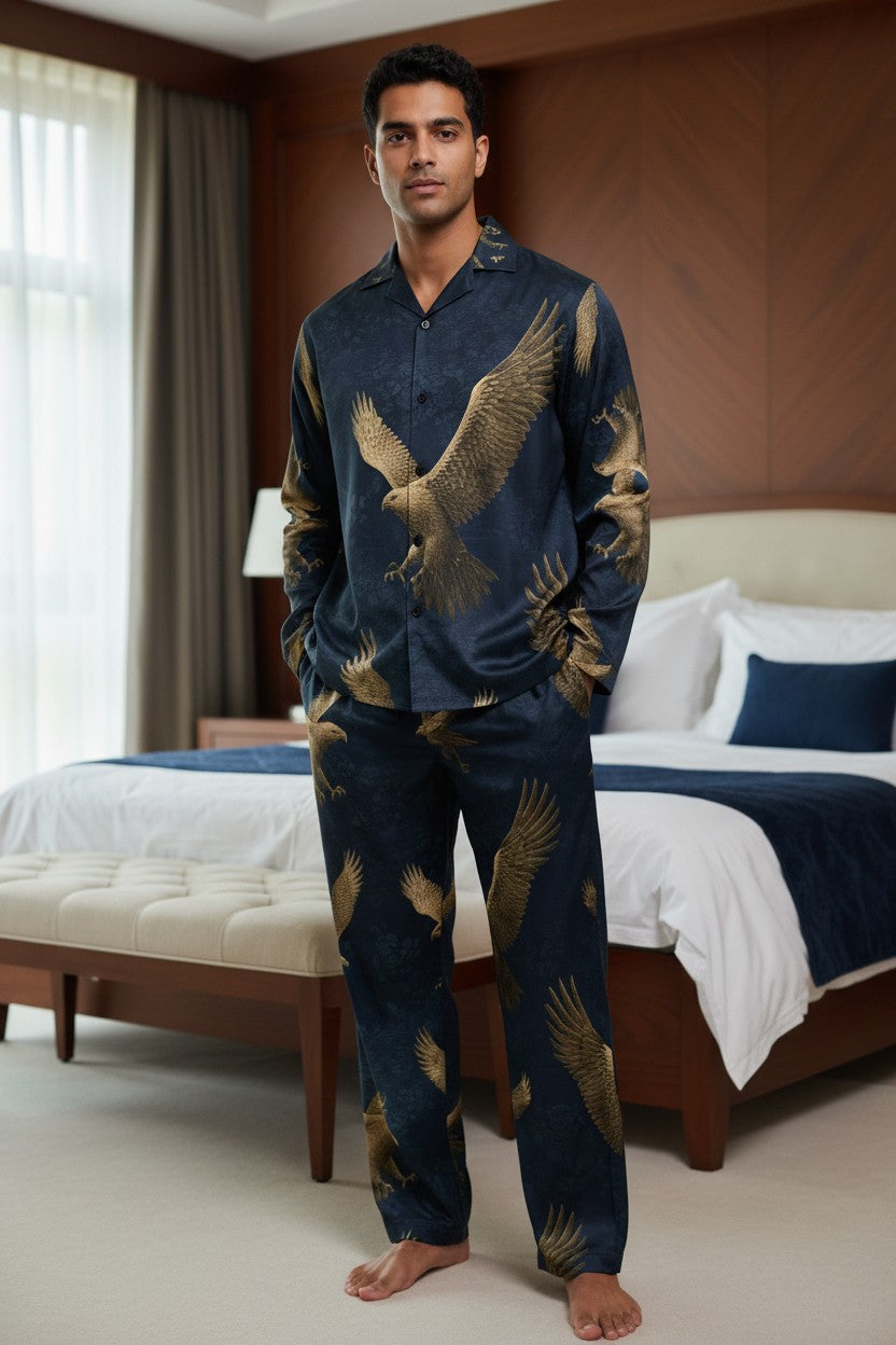 A man wearing a navy blue pajama set with a gold eagle print stands in a bedroom setting.