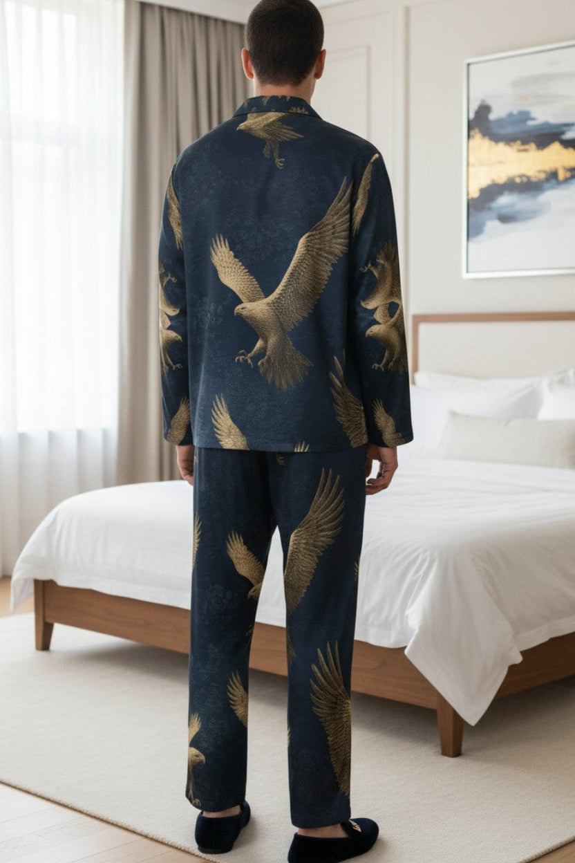 A man stands with his back to the camera in a modern bedroom, wearing a dark navy blue pajama set with a large gold eagle print. The set includes a long-sleeve top and matching pants.