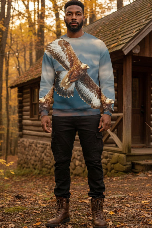 A man wearing a light blue crewneck sweatshirt with a large printed bald eagle graphic, standing in front of a rustic log cabin in an autumn forest.