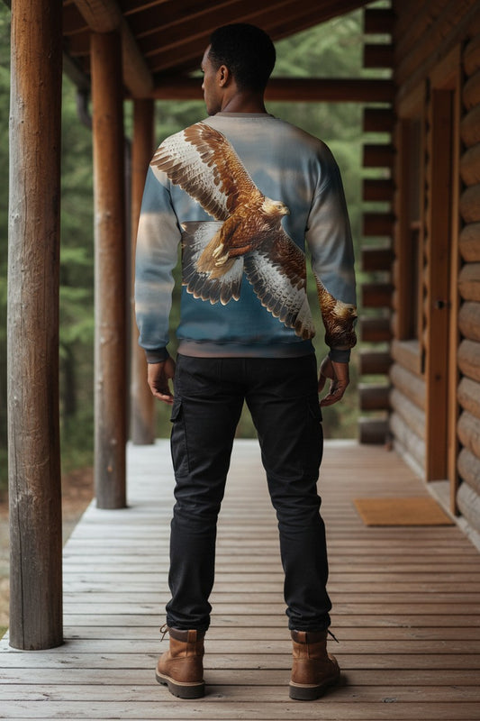 A man viewed from behind wearing a crewneck sweatshirt with a large detailed graphic of a brown and white eagle flying across a blue sky, paired with black pants and brown boots, standing on a wooden porch.
