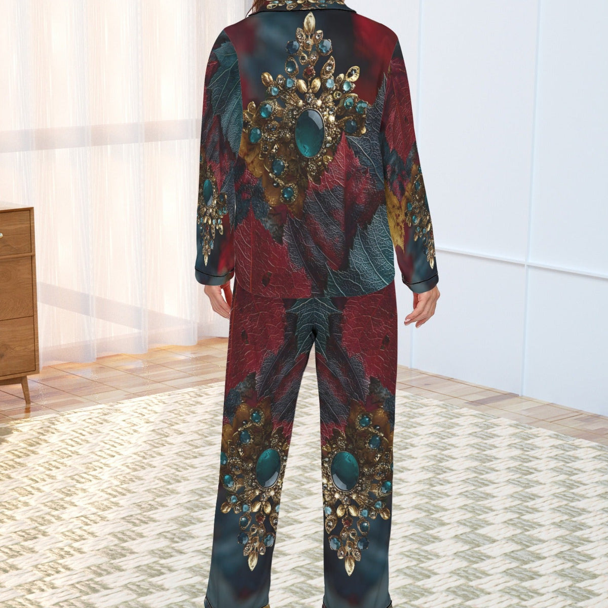 A woman stands with her back to the camera wearing a matching long-sleeve pajama set with an ornate jewel-like abstract print in deep red, teal, and gold tones, set in a bright room with a patterned rug.
