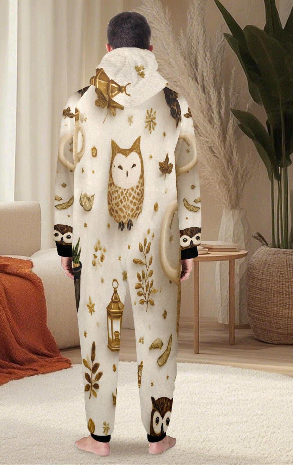 A person standing with their back to the camera wearing a white hooded one-piece pajama or kigurumi with a brown and gold owl and leaf pattern, in a cozy living room setting.