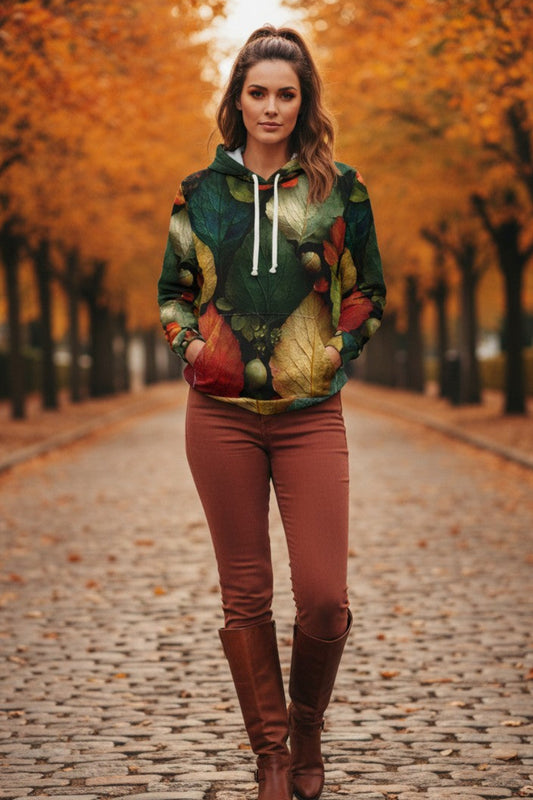 A woman stands on a cobblestone path lined with autumn trees, wearing a colorful leaf-print hoodie, rust-colored pants, and brown knee-high boots.