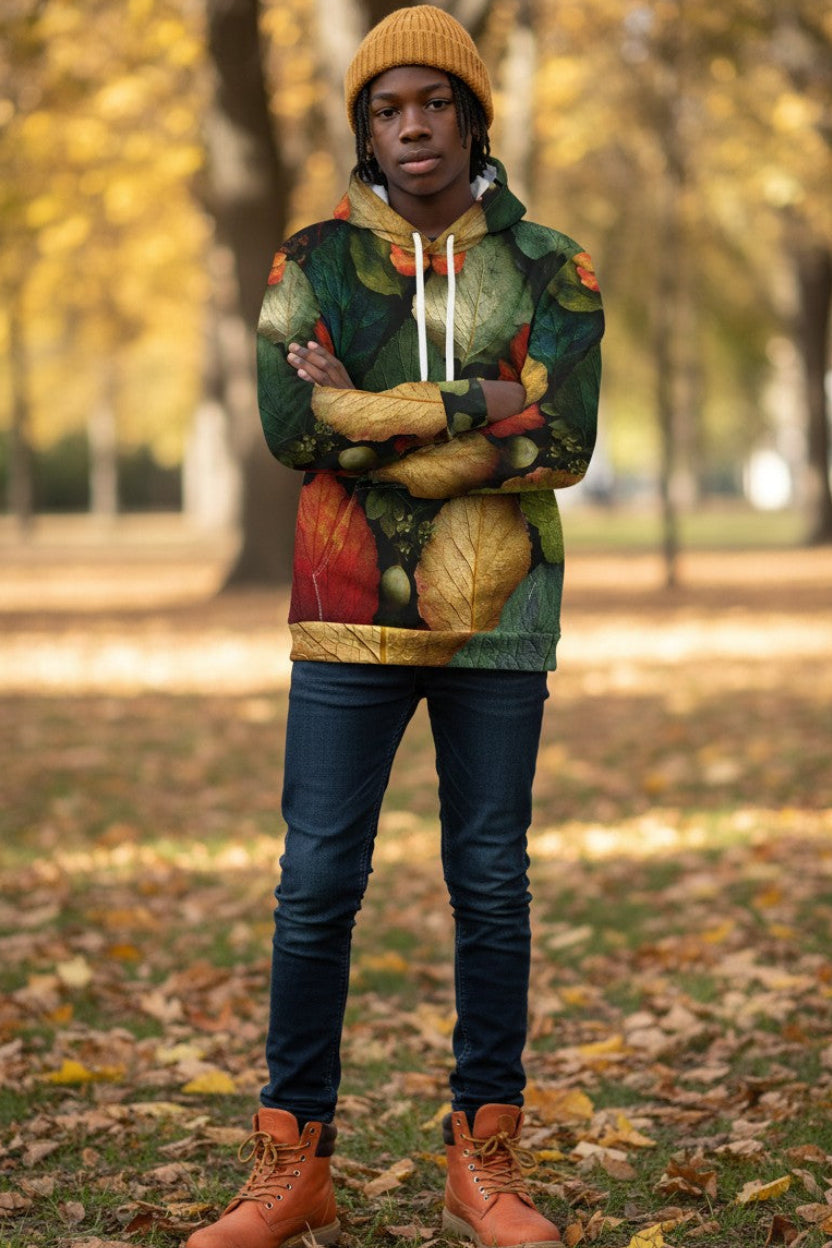 A person standing in an autumn park wearing a colorful hooded sweatshirt with a leaf print, a mustard yellow knit beanie, dark blue jeans, and brown boots.