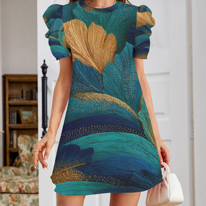 A woman wearing a short-sleeve mini dress with a teal, blue, and gold abstract botanical print, holding a small white handbag in an indoor room setting.