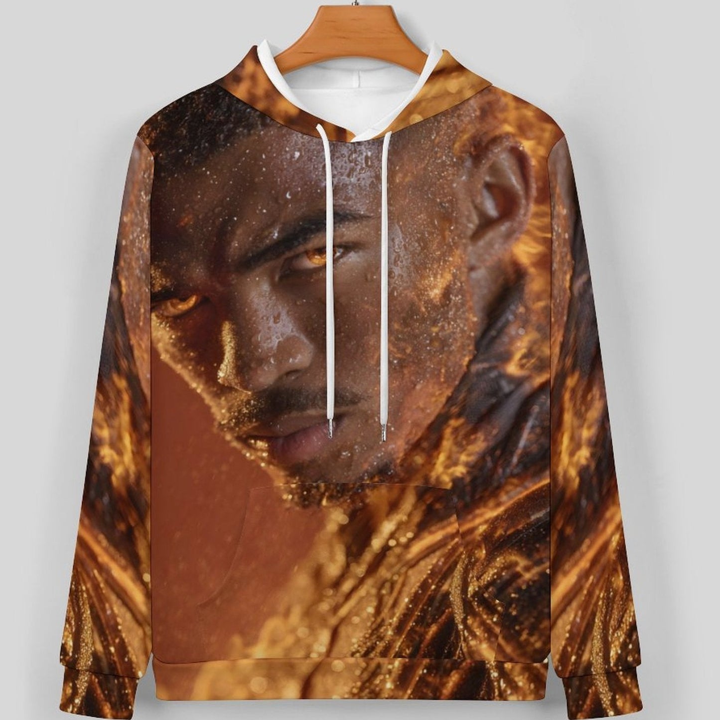 A long-sleeve hoodie with a detailed graphic print of a man's face and fiery textures in shades of brown, gold, and black, featuring white drawstrings and a wooden hanger against a light gray background.