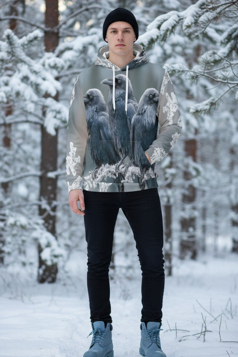 A man wearing a gray and white graphic hoodie with a detailed print of three ravens, standing in a snowy forest.