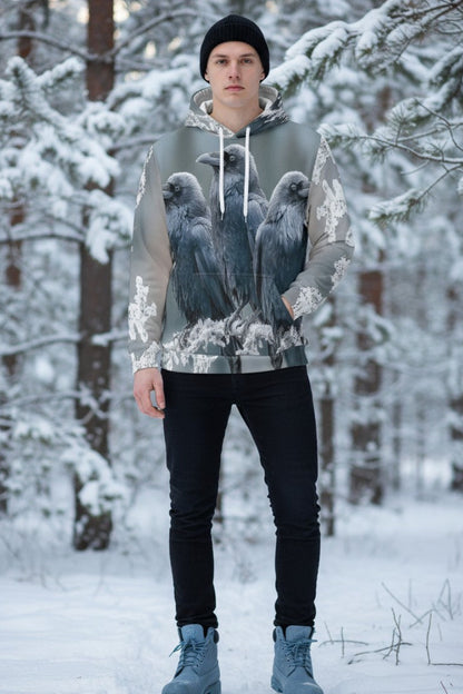 A man wearing a gray and white graphic hoodie with a detailed print of three ravens, standing in a snowy forest.