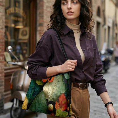 A woman stands on a city street carrying a large tote bag decorated with a detailed print of green leaves and orange-red autumn flowers. She is wearing a dark purple button-up shirt, a beige turtleneck, and brown trousers.