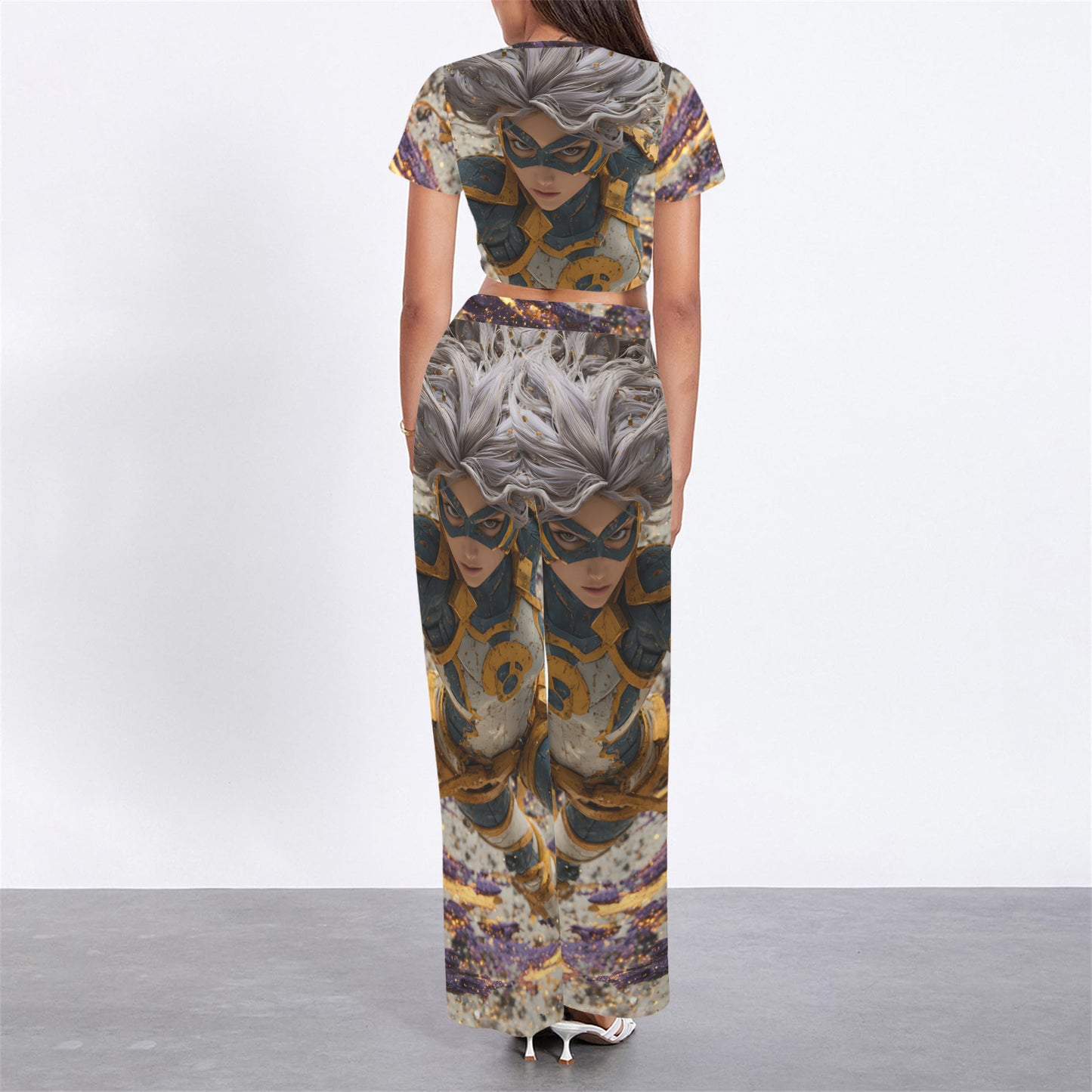 A woman stands with her back to the camera wearing a matching two-piece set consisting of a short-sleeve crop top and wide-leg pants, both printed with a detailed graphic of a masked female character with silver hair.