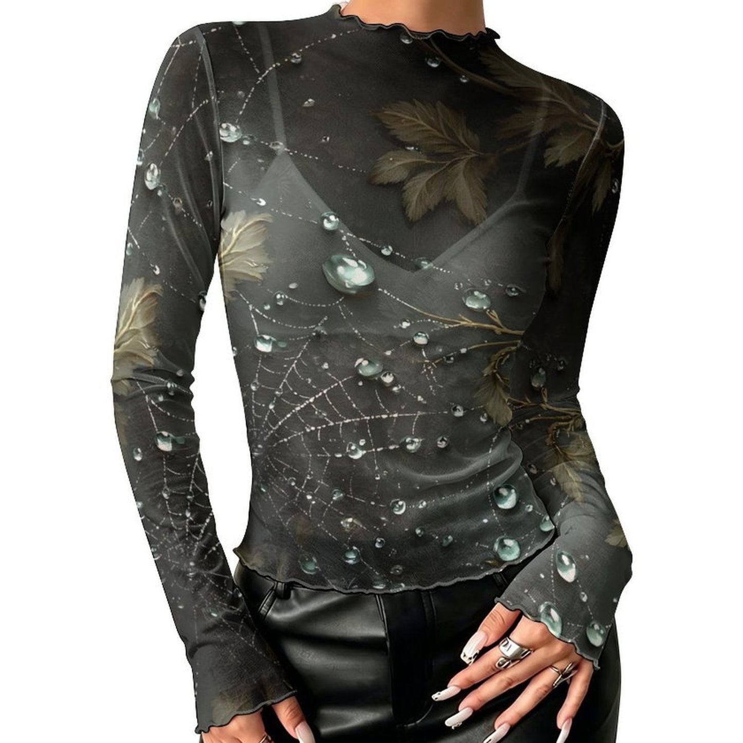 A woman wearing a sheer black long-sleeve top with a spiderweb and dewdrop print, paired with black pants, shown against a plain white background.