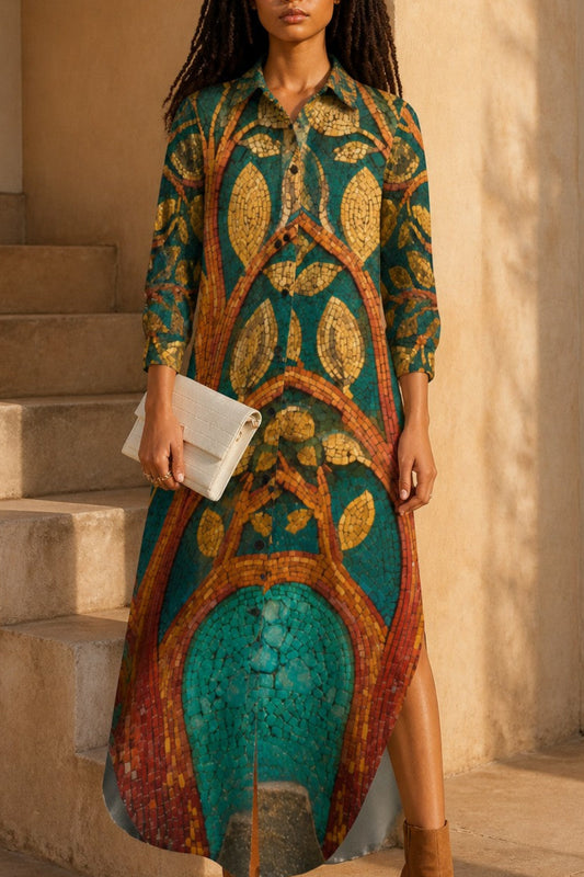 A woman stands on stone steps wearing a long-sleeve button-up dress with a bold tree branch and leaf pattern in teal, gold, and rust tones, holding a white clutch and wearing tan ankle boots.