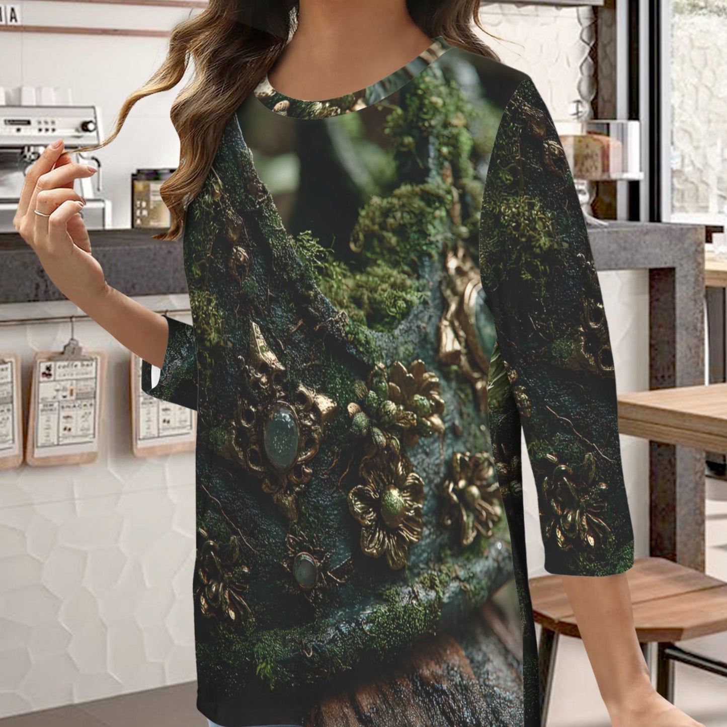 A woman wearing a three-quarter sleeve tunic top with a detailed fantasy print of a mossy tree trunk and gold jewelry, standing in a cafe environment.
