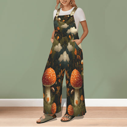 A woman wearing a white t-shirt and dark green wide-leg jumpsuit with a detailed mushroom forest print, standing against a sage green wall.