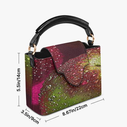A structured handbag with a multicolor abstract print in pink, green, and purple, featuring a black top handle and dimension lines showing its measurements.