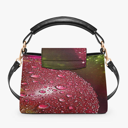 A structured handbag with a black leather top handle and shoulder strap, featuring a front flap and a printed body panel depicting red water droplets on a dark green and purple background.