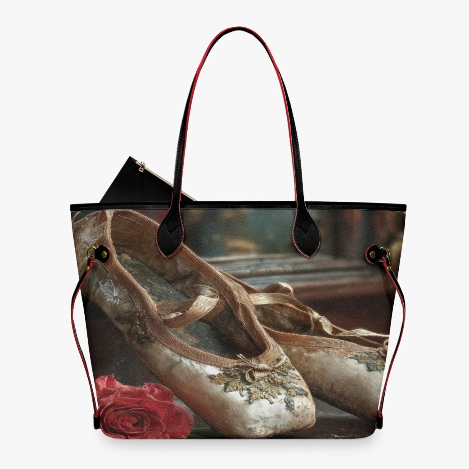 A tote bag featuring a printed design of ballet pointe shoes and a red rose, with black leather handles and trim, shown against a light gray background.