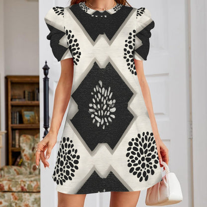A woman wearing a short-sleeve mini dress with a bold black and off-white geometric pattern, holding a small white handbag in an indoor room setting.