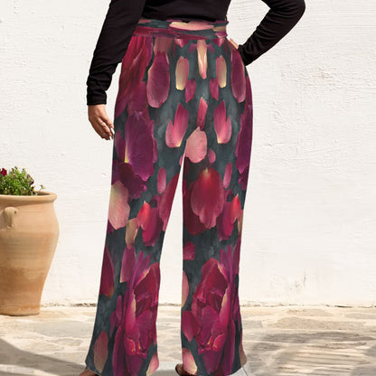 A person wearing high-waisted, wide-leg pants with a dark teal background and large pink and magenta floral print, paired with a black long-sleeve top. The photo is taken outdoors against a white wall with a terracotta planter visible on the left.