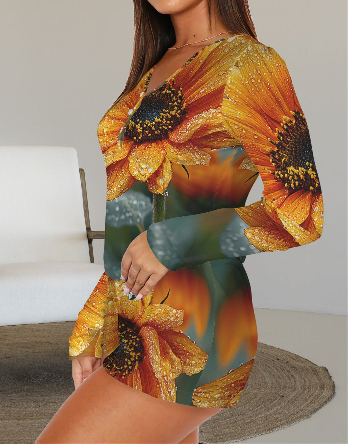 A woman wearing a long-sleeve mini dress with a vibrant sunflower print, standing in a modern room with a white armchair and a round woven rug.