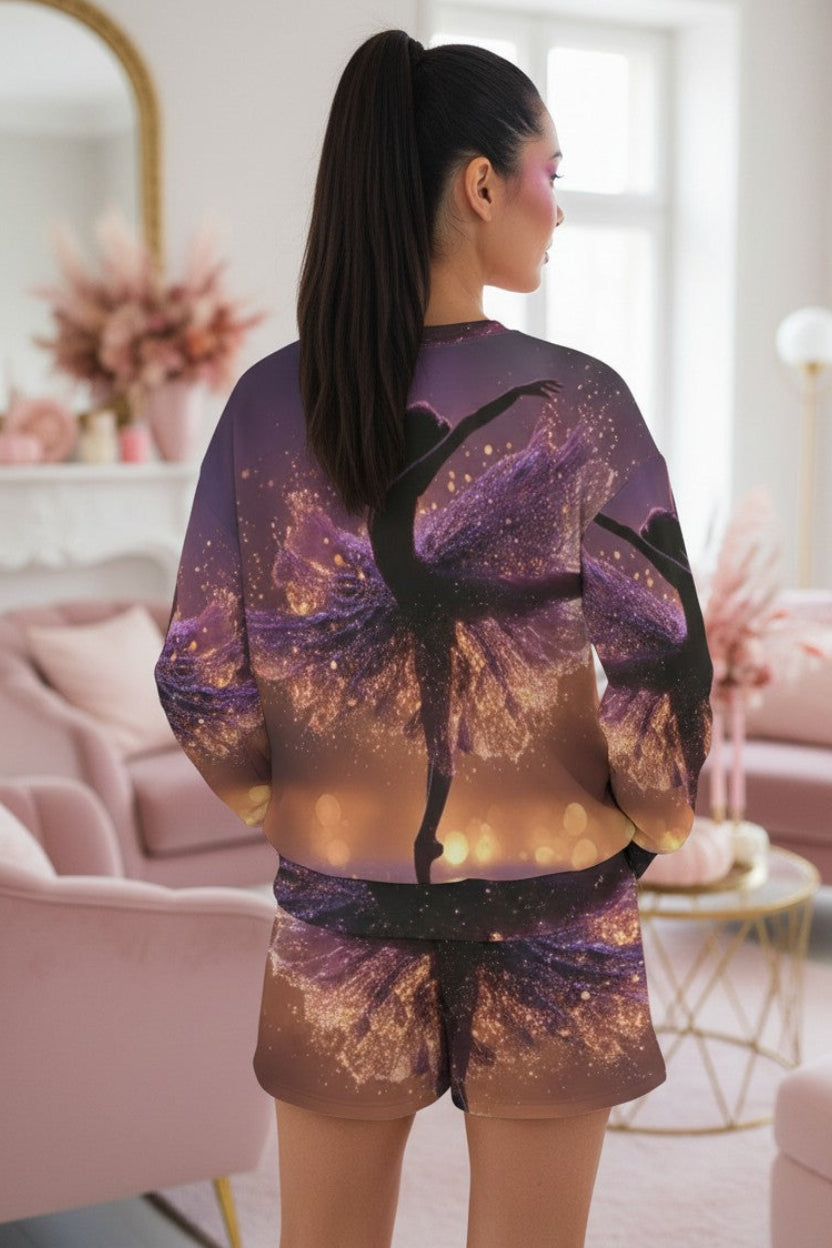 A woman stands with her back to the camera in a bright, pink-toned living room, wearing a matching purple and gold space-themed sweatshirt and shorts set with a black silhouette of a ballerina.
