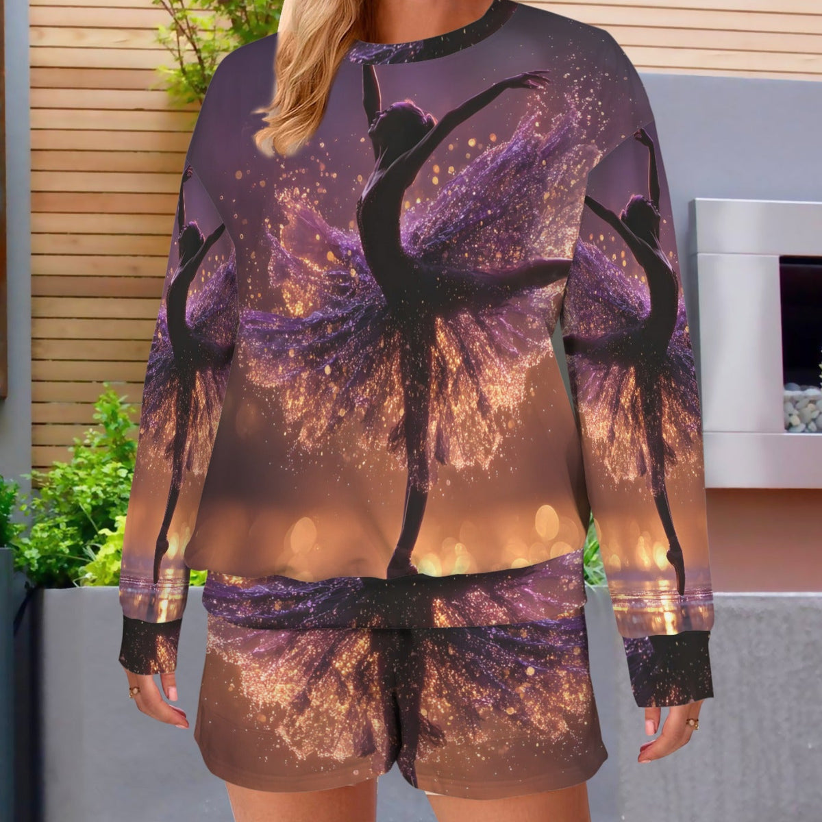 A woman modeling a matching long-sleeve top and shorts set with an all-over print of silhouetted ballerina figures against a purple and gold glittery sunset sky.