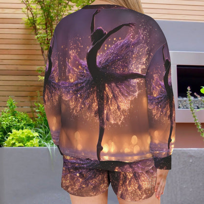 A woman viewed from behind wearing a matching printed lounge set consisting of a long-sleeve top and shorts. The fabric features a purple and gold glittery background with black silhouettes of ballerina dancers.