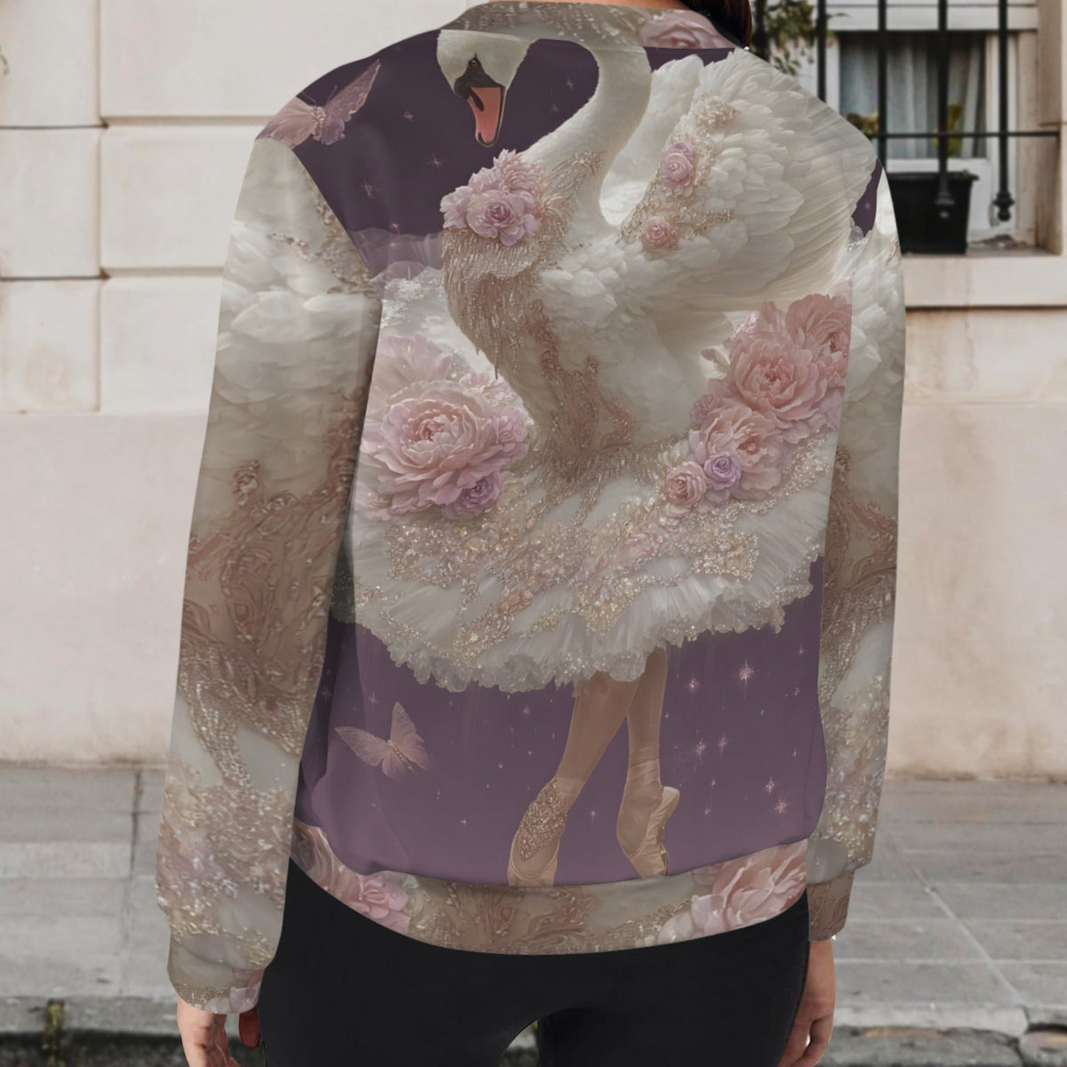 A woman viewed from behind wearing a long-sleeve crewneck sweatshirt with an artistic print of a white swan in a glittery lavender dress decorated with pink roses, set against a city street background.