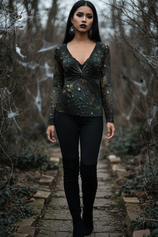 A woman stands on a stone path in a wooded outdoor setting wearing a dark long-sleeve V-neck top with a twisted front detail and black leggings.