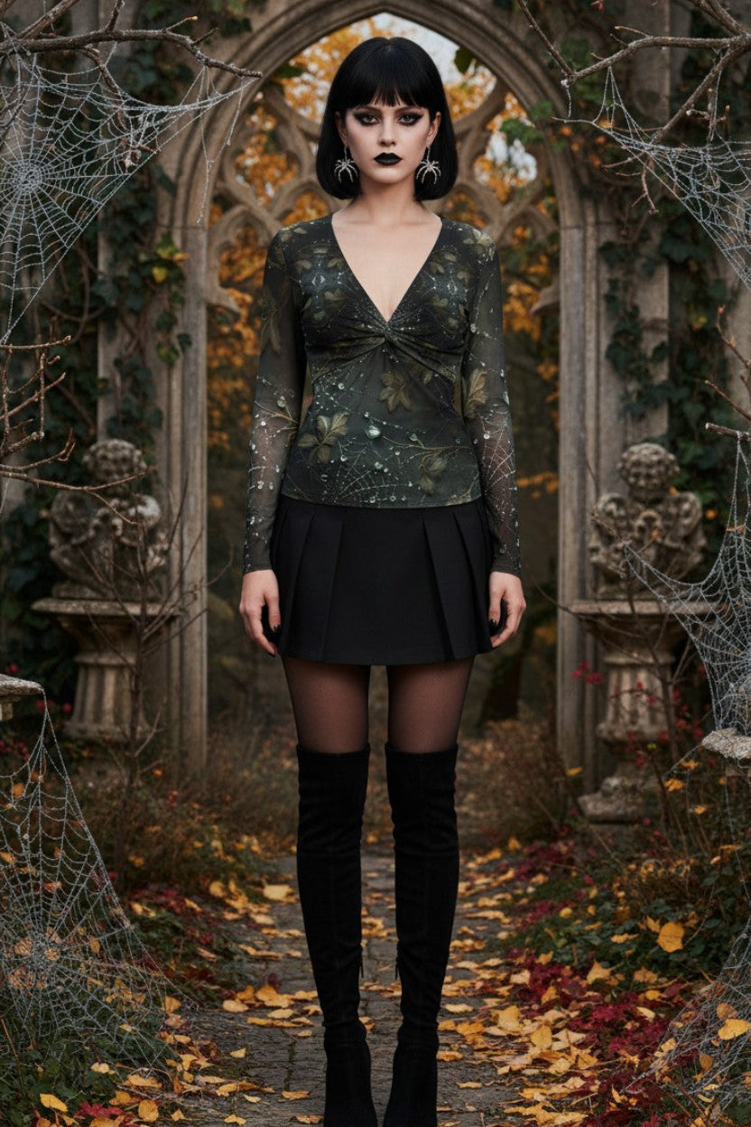 A gothic-style woman stands in a stone archway surrounded by cobwebs and fallen leaves, wearing a dark patterned long-sleeve top, a short black skirt, sheer black tights, and black knee-high boots.