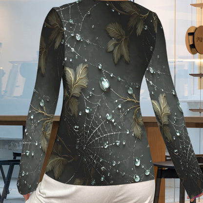 A woman shown from the back wearing a long-sleeve top with a dark gray and black spiderweb and leaf pattern, featuring realistic water droplets, paired with white pants in a modern cafe setting.