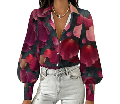 A woman wearing a long-sleeve button-up blouse with a bold floral print in deep pink, burgundy, and dark green, paired with light-wash jeans and a gold chain necklace, shown against a plain white background.